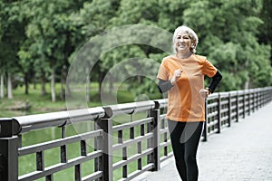 Athletic asian senior woman running outdoor jogging in park.