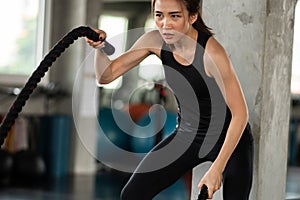 Athletic asian woman exercising with battle rope at gym