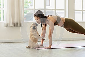 Athletic Asian woman practice yoga Plank pose to meditation and kissing dog pug breed at home