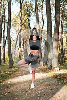 Athletic attractive woman performs a variation of vrikshasana exercise, tree pose with arms raised
