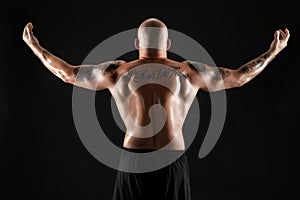 Athletic bald, bearded, tattooed man in black shorts is posing against a black background. Close-up portrait.