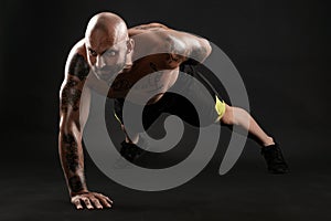 Athletic bald, tattooed man in black shorts and sneakers is posing against a black background. Close-up portrait.