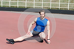 Athletic bearded man with muscular body stretching on running track