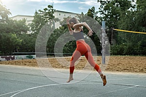 Athletic beautiful middle-aged woman in black and red fitness clothes runs on the sports ground