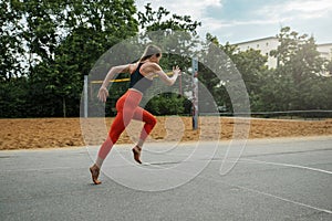 Athletic beautiful woman in black red fitness clothes, runs on the sports ground