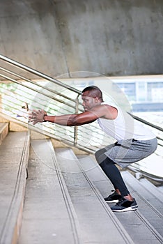 Athletic Black American men in a sport wear are exercising outdoors by doing squats.