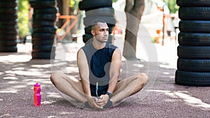 Athletic black guy stretching on asphalt road after his morning workout at park