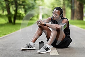 Athletic black man sitting on park way, checking on smartwatch