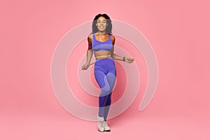athletic black woman in purple activewear measures waist in studio