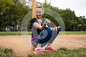 Athletic blonde girl is sitting near the goal post of football goal. And points a finger at the frame