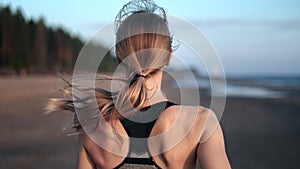 Athletic blonde woman with waving hair running jogging cardio training at sea beach back view slowmo