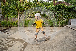 Athletic boy in helmet and knee pads learns to skateboard with in a skate park. Children education, sports