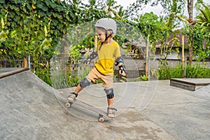 Athletic boy in helmet and knee pads learns to skateboard with in a skate park. Children education, sports