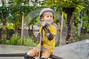 Athletic boy in helmet and knee pads learns to skateboard with in a skate park. Children education, sports