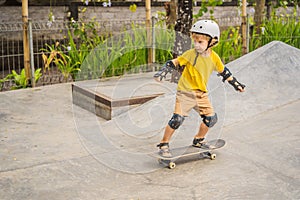 Athletic boy in helmet and knee pads learns to skateboard with in a skate park. Children education, sports