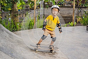 Athletic boy in helmet and knee pads learns to skateboard with in a skate park. Children education, sports