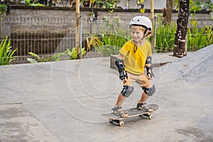 Athletic boy in helmet and knee pads learns to skateboard with in a skate park. Children education, sports