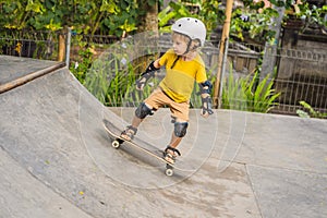 Athletic boy in helmet and knee pads learns to skateboard with in a skate park. Children education, sports