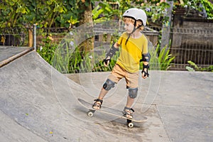 Athletic boy in helmet and knee pads learns to skateboard with in a skate park. Children education, sports