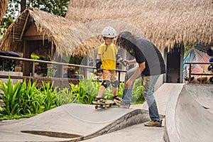 Athletic boy learns to skateboard with asian trainer in a skate park. Children education, sports. Race diversity