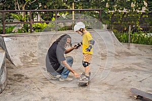 Athletic boy learns to skateboard with a trainer in a skate park. Children education, sports