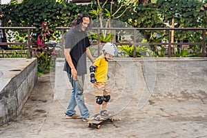 Athletic boy learns to skateboard with a trainer in a skate park. Children education, sports