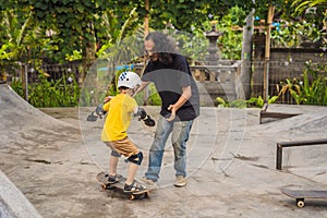 Athletic boy learns to skateboard with a trainer in a skate park. Children education, sports