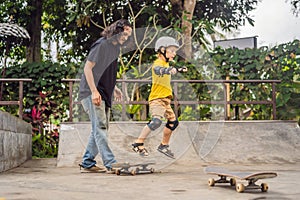 Athletic boy learns to skateboard with a trainer in a skate park. Children education, sports