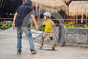 Athletic boy learns to skateboard with a trainer in a skate park. Children education, sports