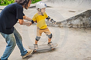 Athletic boy learns to skateboard with a trainer in a skate park. Children education, sports