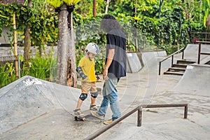 Athletic boy learns to skateboard with a trainer in a skate park. Children education, sports