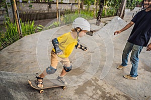 Athletic boy learns to skateboard with a trainer in a skate park. Children education, sports