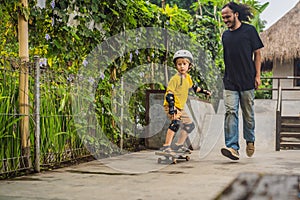 Athletic boy learns to skateboard with a trainer in a skate park. Children education, sports