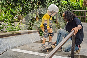 Athletic boy learns to skateboard with a trainer in a skate park. Children education, sports