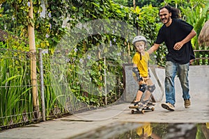 Athletic boy learns to skateboard with a trainer in a skate park. Children education, sports