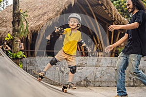 Athletic boy learns to skateboard with a trainer in a skate park. Children education, sports