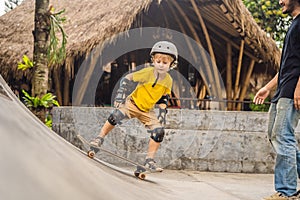 Athletic boy learns to skateboard with a trainer in a skate park. Children education, sports