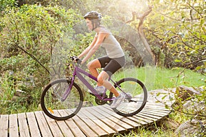 Athletic brunette mountain biking on wooden path