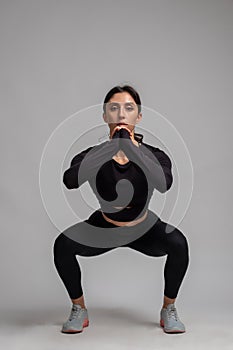 Athletic brunette performing bodyweight squats on grey background