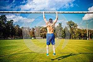 Athletic built man doing chinups and core training in park. Fitness football player training on grass court, hardcore training