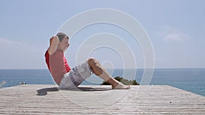 Athletic Caucasian man pumps the abdominals on rocky coast beach on sunny day