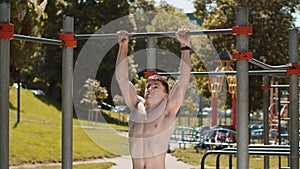 Athletic caucasian topless muscular man doing pull ups exercises on horizontal bar, pumping up back