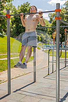 Athletic caucasian topless muscular man doing pull ups exercises on horizontal bar, pumping up back