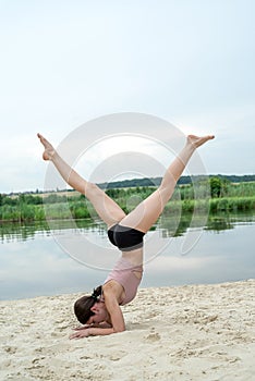 athletic caucasian woman in sport wear is practicing yoga on lake sand beach