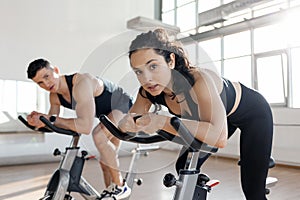 athletic couple of cyclists train on static bicycle simulator, man trainer and fitness woman go in for sports together