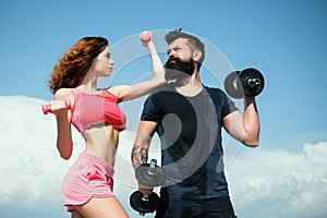 Athletic couple of fit man and woman with a dumbells outdoors. Couple doing fitness outside. Young fitness couple.