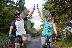 Athletic couple giving high five while riding bicycle on the road