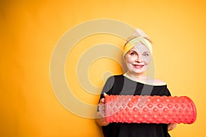 Athletic elderly woman with sports bandage on her head holding fascia in her hands and smiling