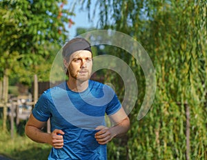 Athletic european man in sportswear jogging on road in green park on beautiful summer day