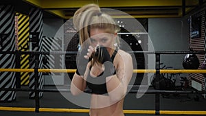 Athletic female kickboxer practices kicking in the boxing ring in the gym.